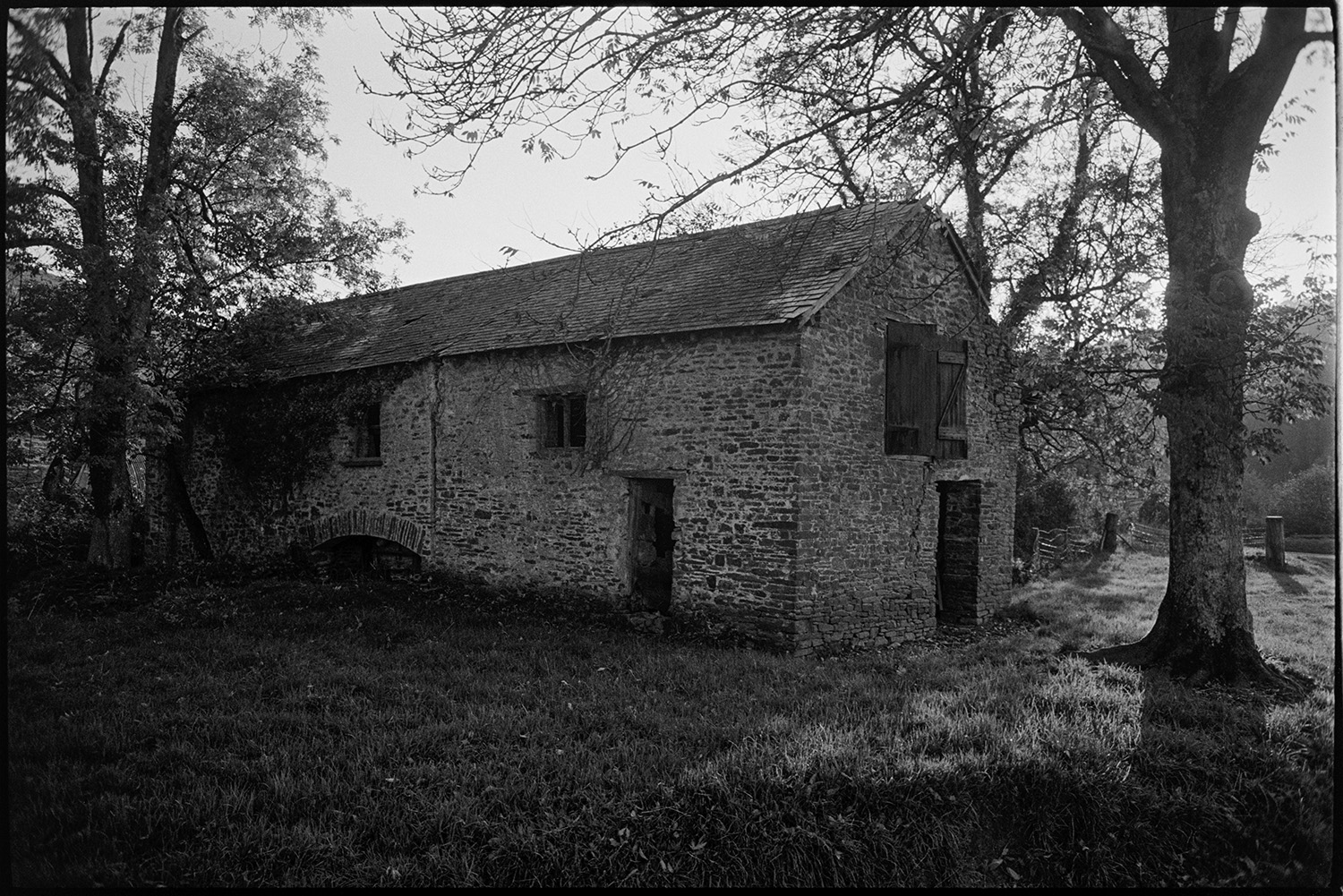 Old mill with rotting wheel stone built. 
[The stone water mill building with a tallet at Cawseys Meethe, Kings Nympton. The building is surrounded by trees.]