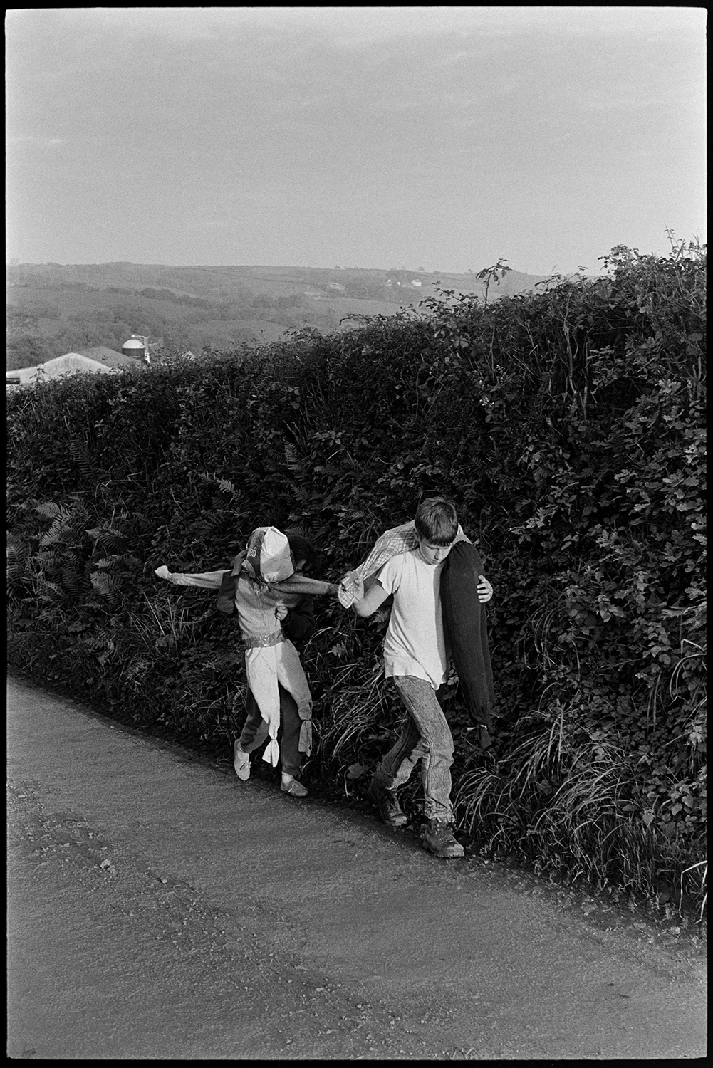 Children walking down lane carrying guy. 
[Two children walking down a lane near Spittle farm, Chulmleigh, each carrying an effigy of Guy Fawkes for bonfire night.]