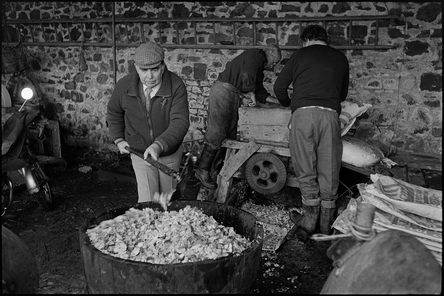 Cider making, apple crusher and cider press. 
[Bill Hammond and another man pulping apples for cider making using an apple crusher at the back of a barn at Rashleigh Mill, Bridge Reeve. Another man is shovelling the pulp into a barrel in the foreground.]