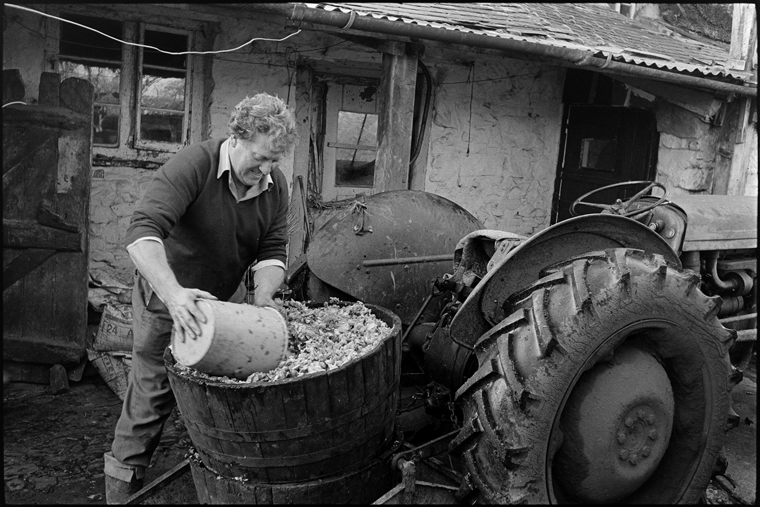 Cider making, apple crusher and cider press. 
[A man scooping apple pulp out of a barrel attached to a tractor, with a bucket, at Rashleigh Mill, Bridge Reeve.]