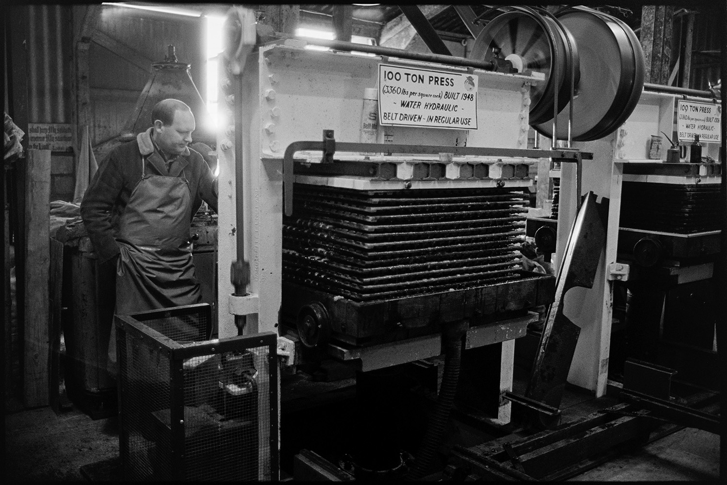 Cider making, men operating cider press in factory. 
[A man working a 100 ton cider press built in 1948, at Hancock's cider factory at Clapworthy Mill, South Molton.]