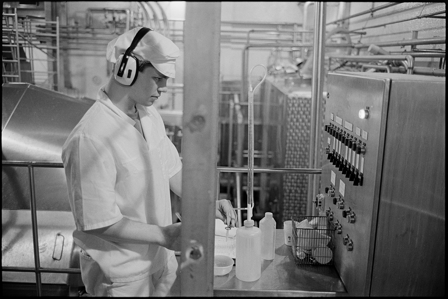 Men working in cheese factory. 
[A man testing cheese at the Dairy Crest North Tawton Cheese Factory. He is wearing ear defenders.]
