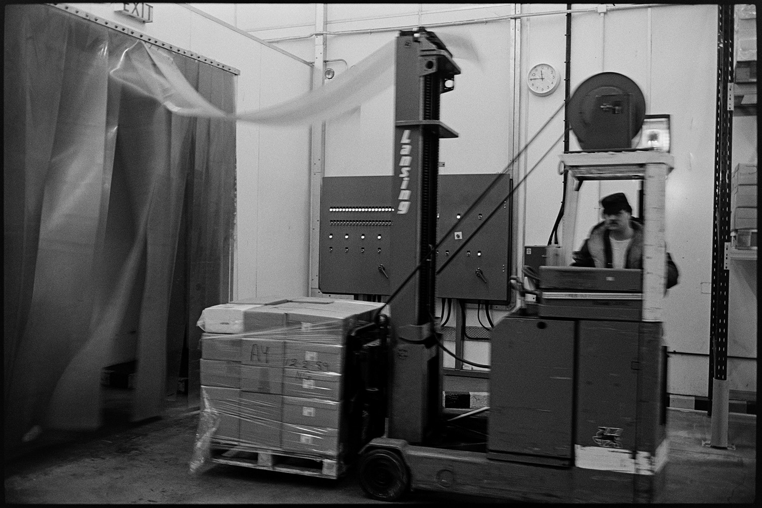 Men working in cheese factory. 
[A man operating a fork lift truck carrying boxes at the Dairy Crest North Devon Cheese Factory.]