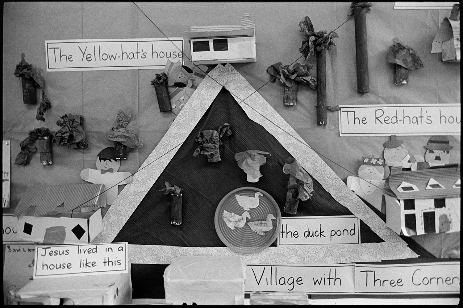 Children in primary school prefab classroom, before move to new school. 
[A display of children's artwork titled 'Village with Three Corners' in a classroom at Chulmleigh primary School.]