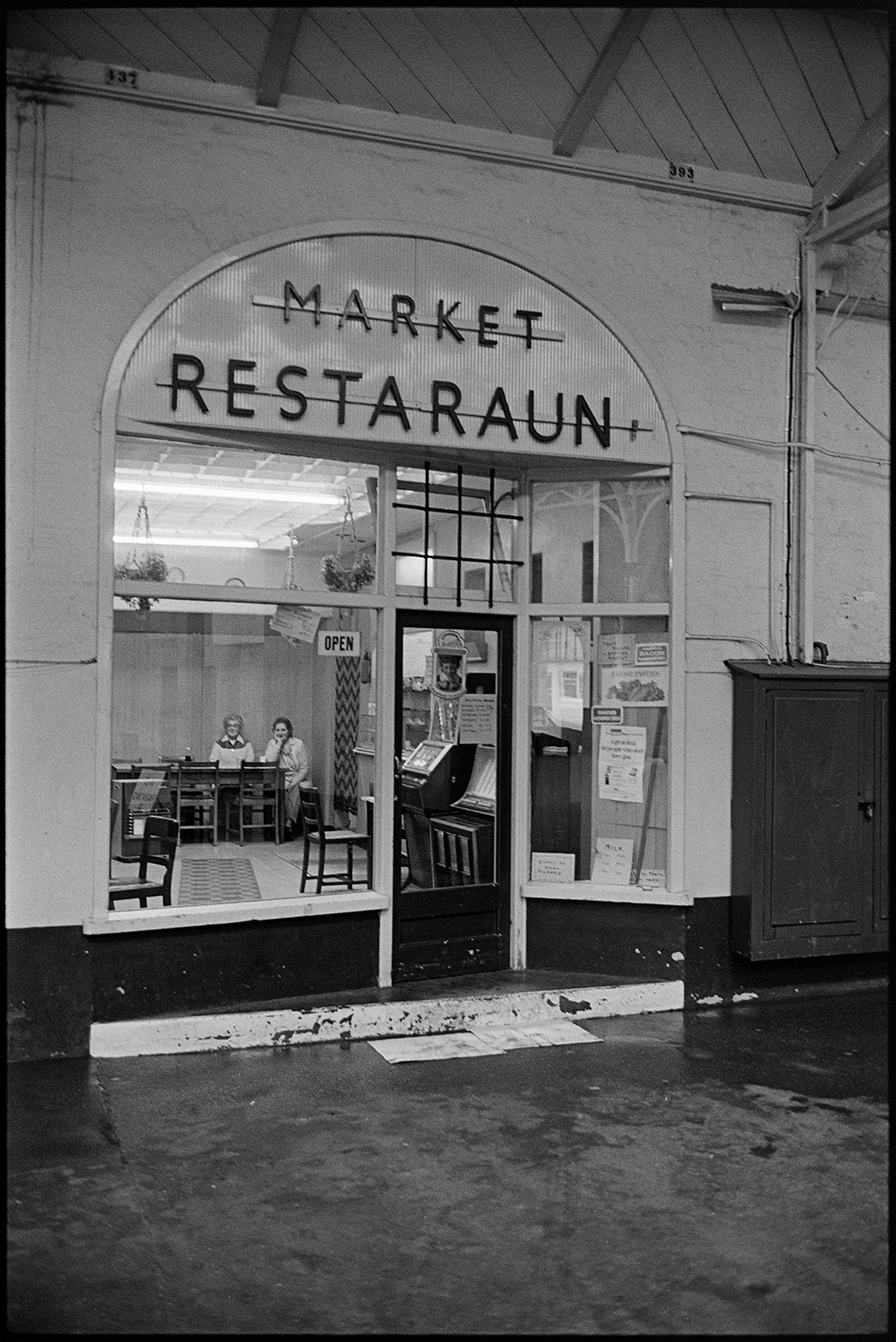 Restaurant in pannier market, front of. 
[The front of the 'Market Restaurant' in Barnstaple Pannier Market. Two people can be seen sitting inside.]