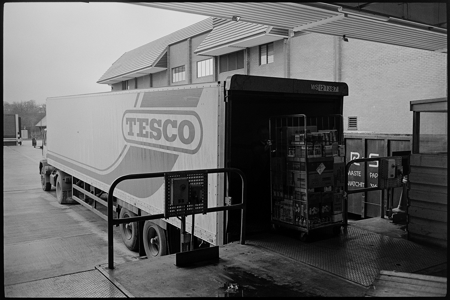 Interior of supermarket with people shopping, delivery lorry being unloaded. 
[Goods being unloaded from a lorry at the Tesco supermarket in Barnstaple.]