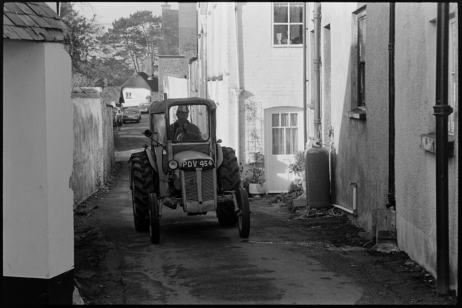 A tractor being driven along a lane behind a row of houses, possibly in Chulmleigh.