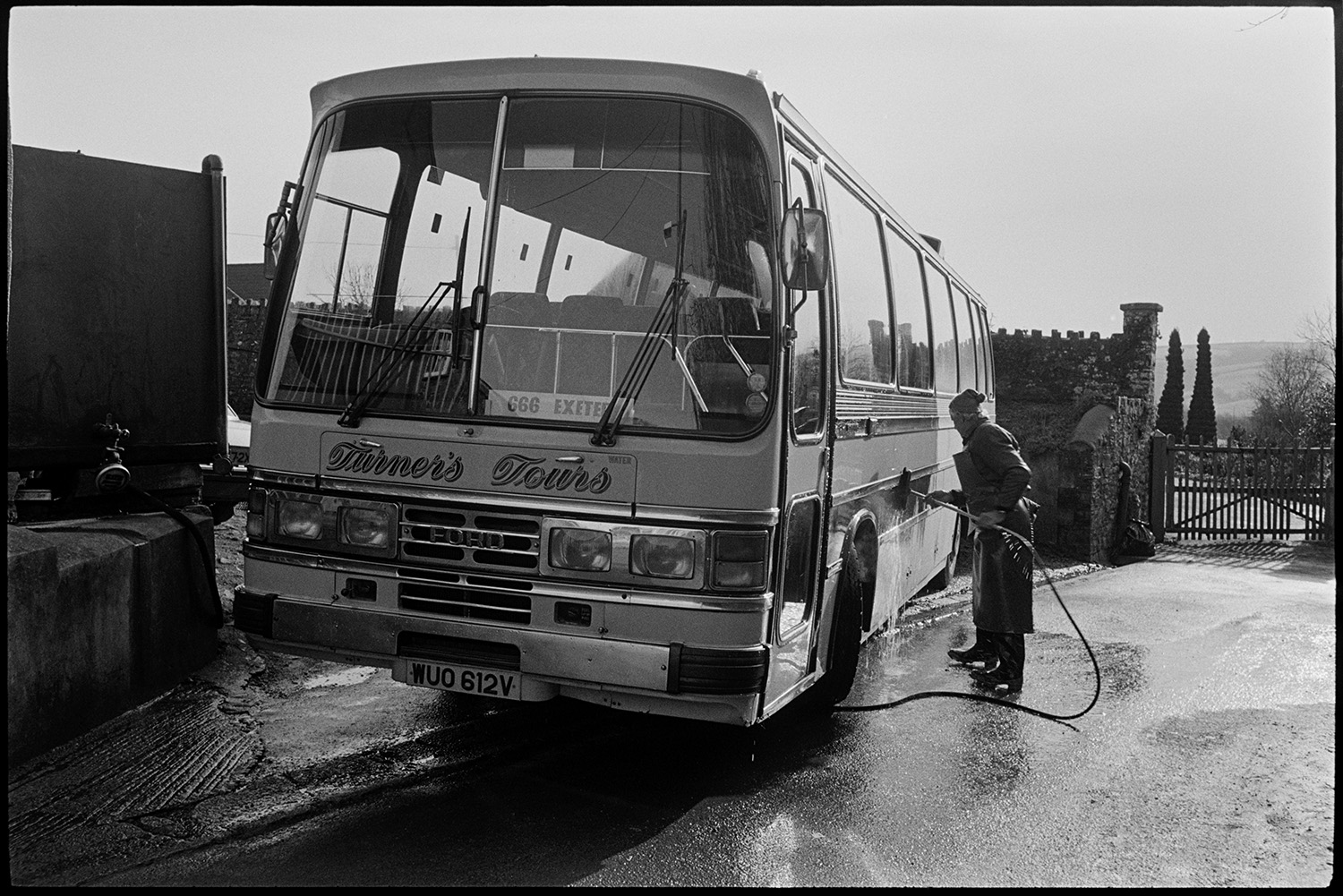 Man cleaning bus with hose. 
[A man washing a Turners Tours coach with a hose and brush in Chulmleigh.]