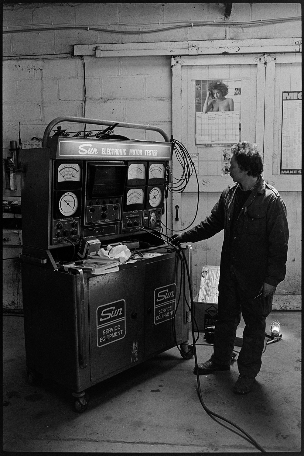 Interior of garage with car being serviced.
[The interior of the workshop at the Taw Valley Garage near Eggesford, with Martin Perron standing beside an electronic motor testing machine.]