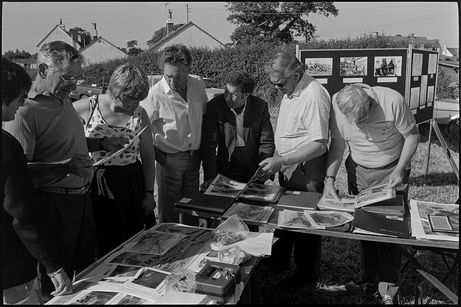 Country fair, majorettes, cups on display, stalls.
[Men and women looking through photographs from the Beaford Archive displayed on an outside table at  Ashreigney Country Fair. There are also display boards in the background with more photographs.]
