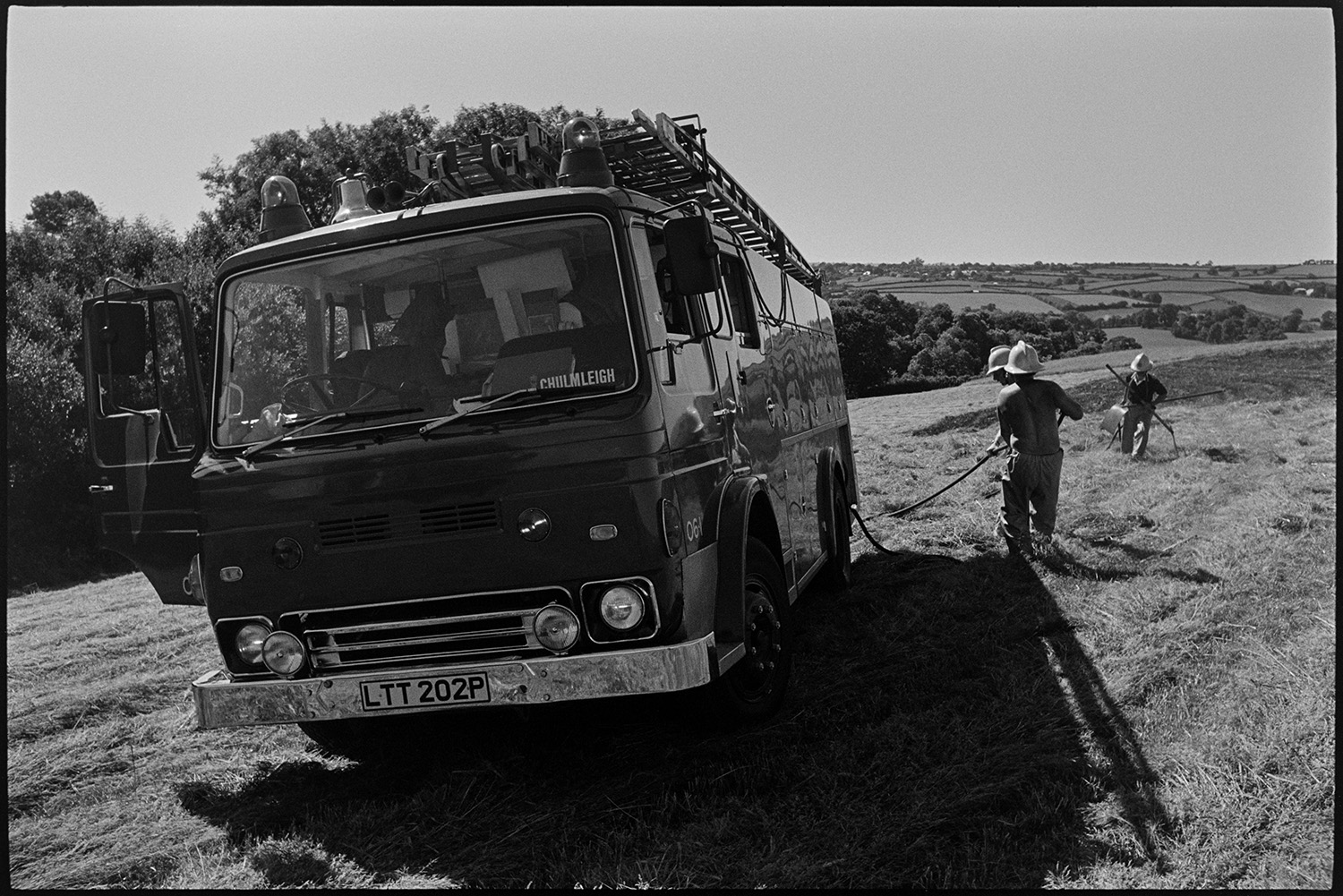 Firemen damping down field after crop fire. Fire engine parked in field.
[Firemen damping down smouldering embers after hosing down a crop fire in a field near Chawleigh. A fire engine is parked in the field.]