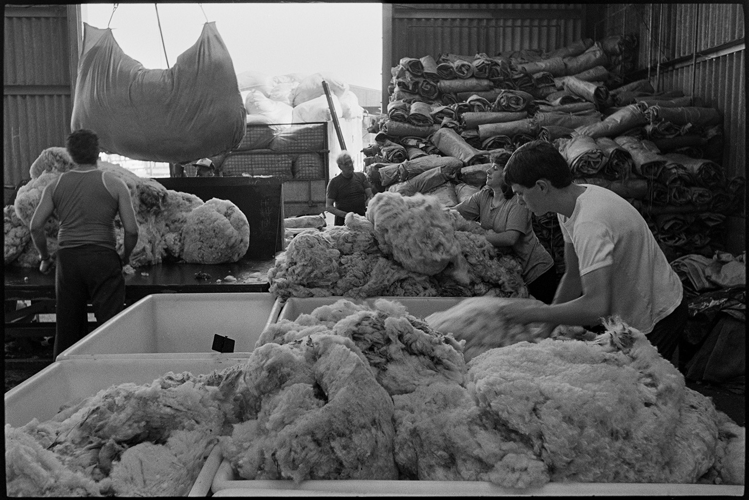 Men sorting and packing wool in warehouse.
[Three men and a woman sorting and packing wool in a warehouse operated by Devon & Cornwall Wools Ltd at the Pathfields Business Park in South Molton.]