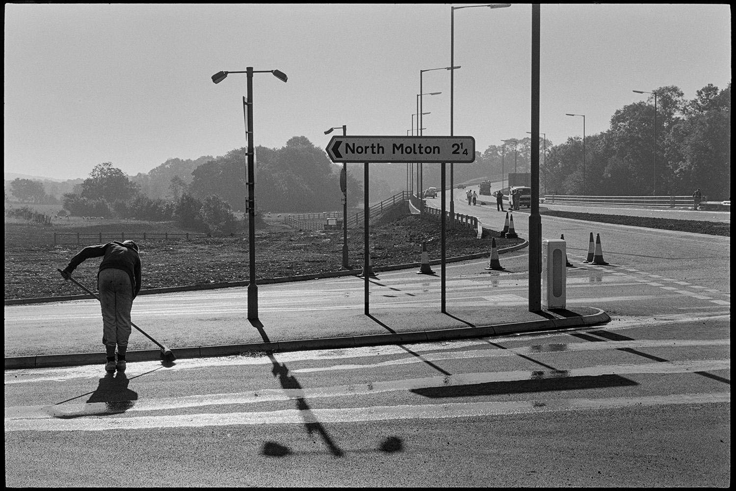 Men clearing new link road before official opening.
[Man sweeping the road at the junction of the North Molton Road and the A361 North Devon Link Road near South Molton, before the official opening of the road. In the background other workers and vehicles can be seen on the road.]