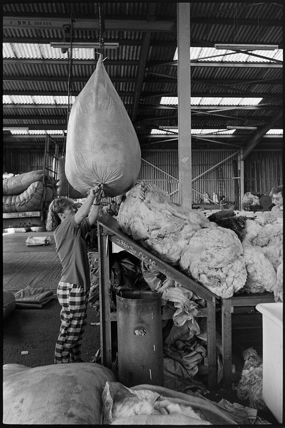 A woman opening a bag of wool which is suspended from a hoist, in the warehouse of Devon & Cornwall Wools Ltd at the Pathfields Business Park in South Molton.