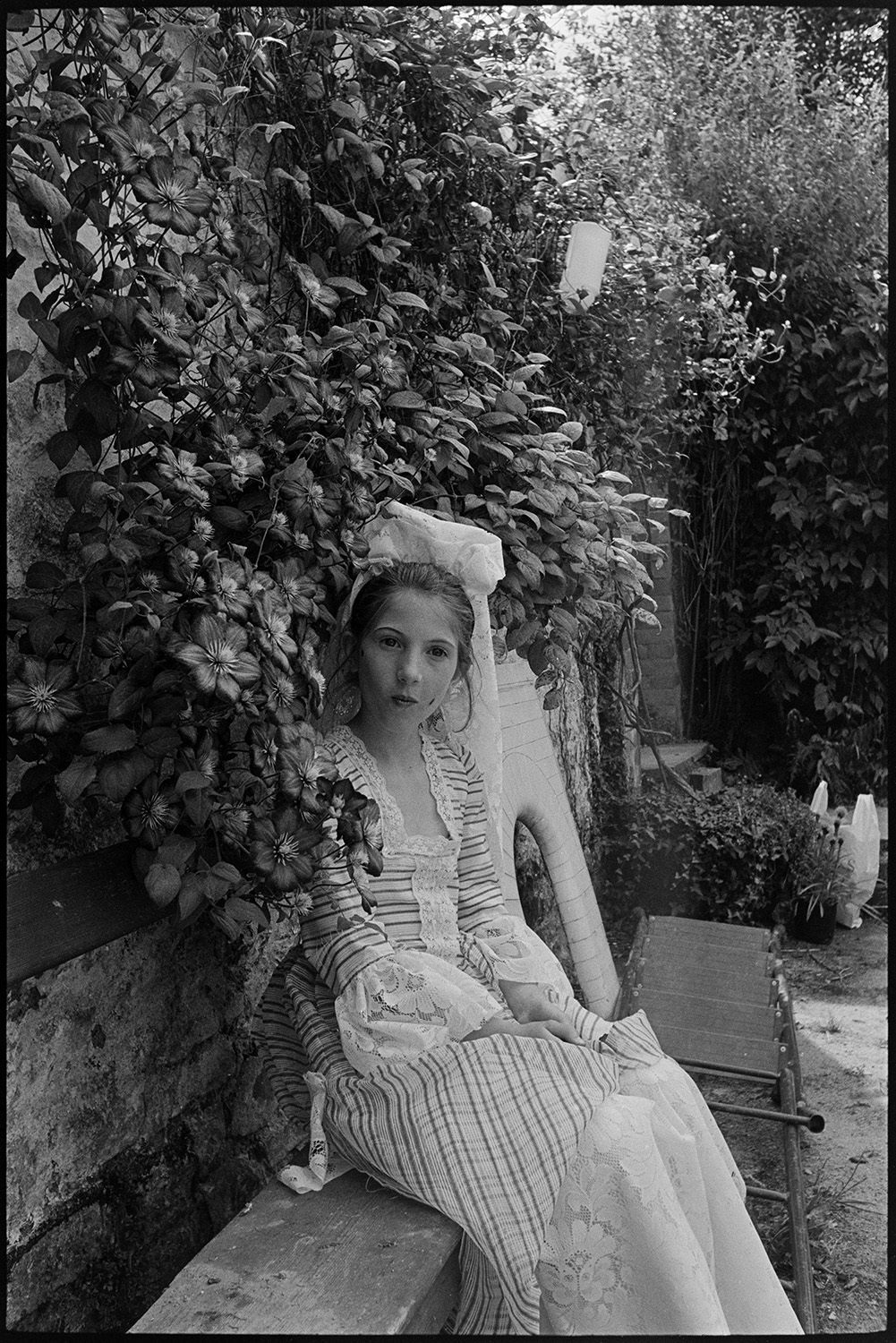 Portrait of dressed for carnival. 
[Camilla Robinson in fancy dress sat on a bench by a wall covered in foliage at North Walk, Chulmleigh for Chulmleigh Fair.]