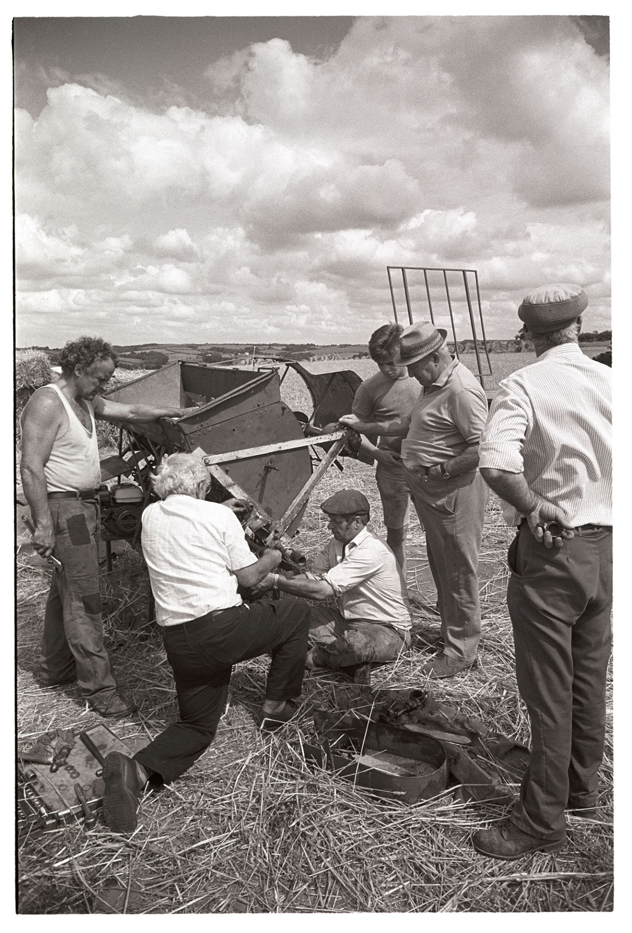 Reed combers mending fault in tying machine attached to reed comber. 
[Men fixing the tying machine attached to a reed comber in a field at Spittle, Chulmleigh, while they are harvesting.]