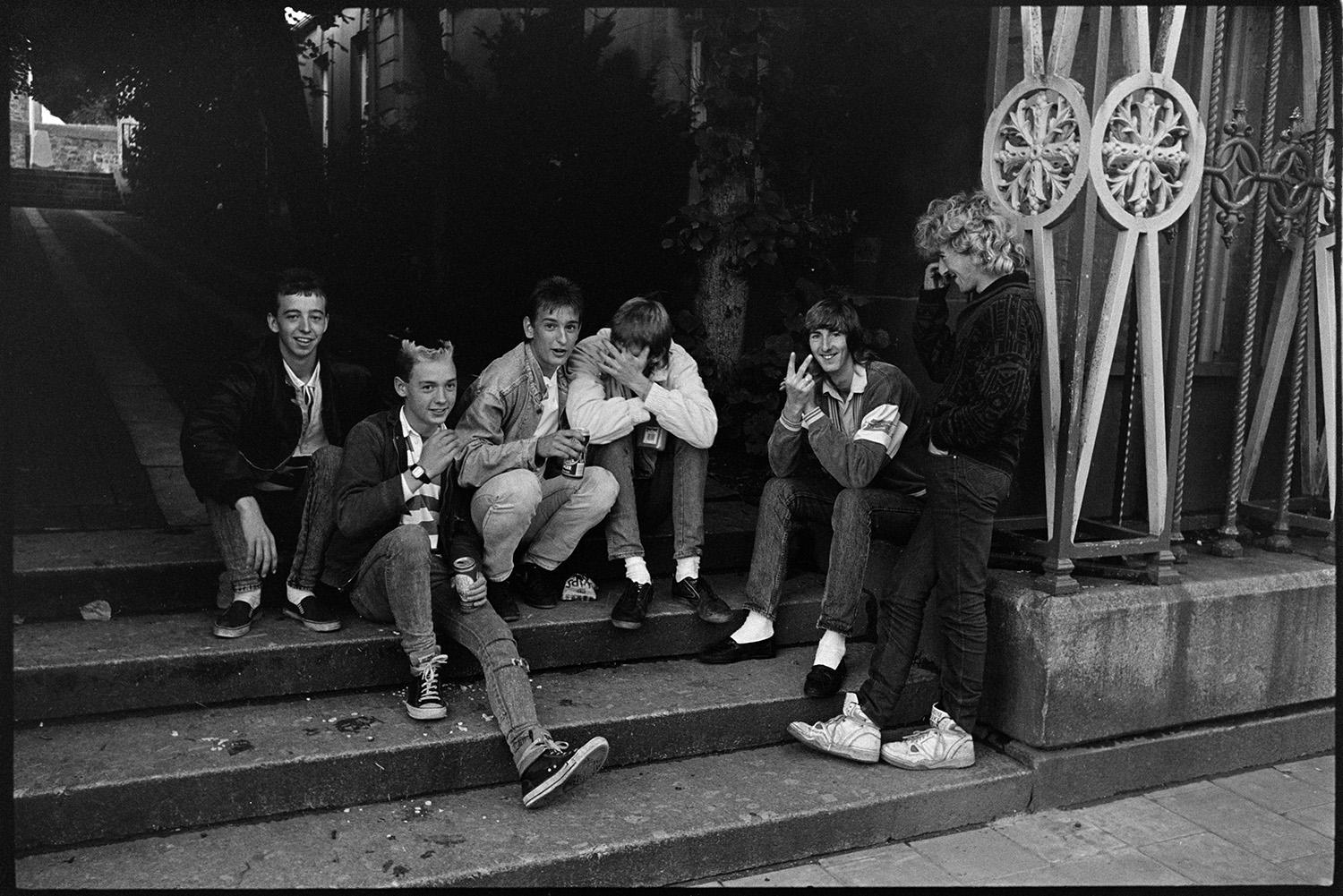 Spectators waiting for start of fair in town square. 
[A group of teenagers sitting on the steps leading towards South Molton church, waiting for the fair to start.]