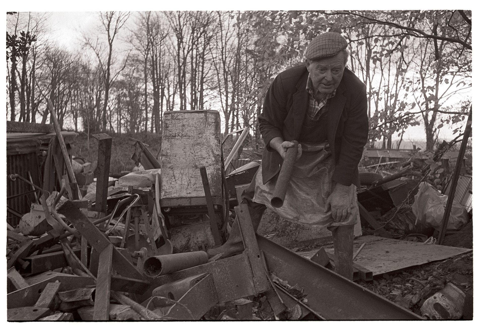Scrap metal merchant working in his yard, chatting to photographer. 
[Jimmy Hughes, a scrap metal merchant sorting scrap metal in his yard at Leigh Road, Chulmleigh.]