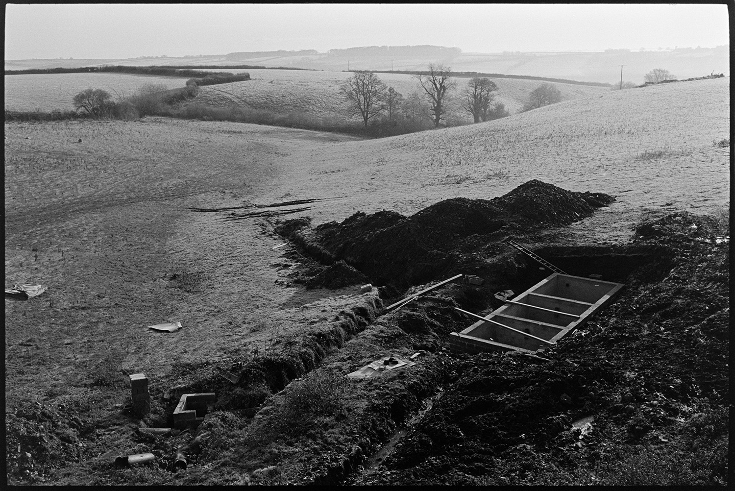 Slurry pit under construction. 
[The foundations of a slurry pit in a field at Parsonage Farm, Chulmleigh. A landscape of fields, hedgerows and trees can be seen in the background.]