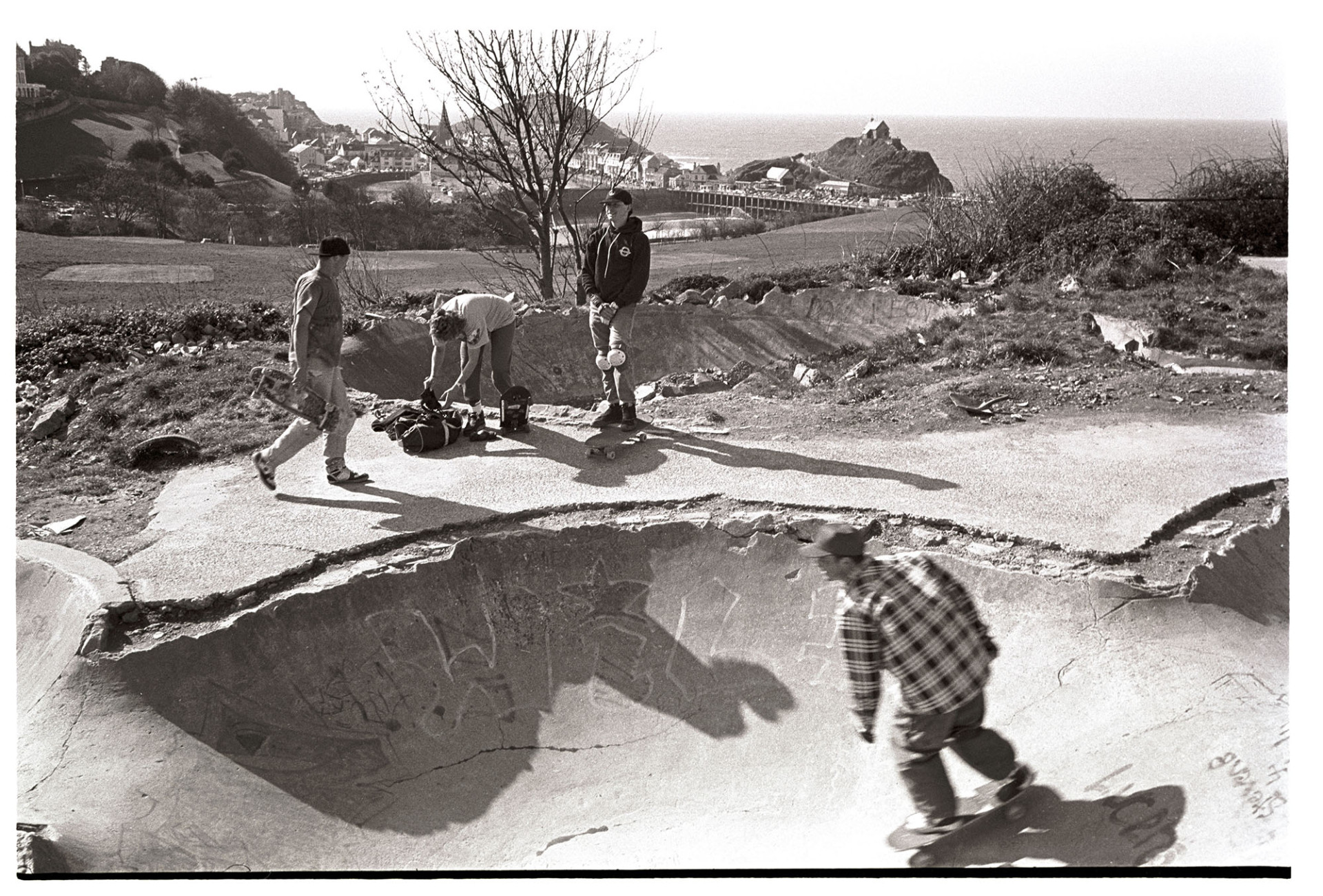 Skateboarders at skate park near sea. <br />
[Young men skateboarding at a skate park in Ilfracombe. The sea and town of Ilfracombe are visible in the background.]