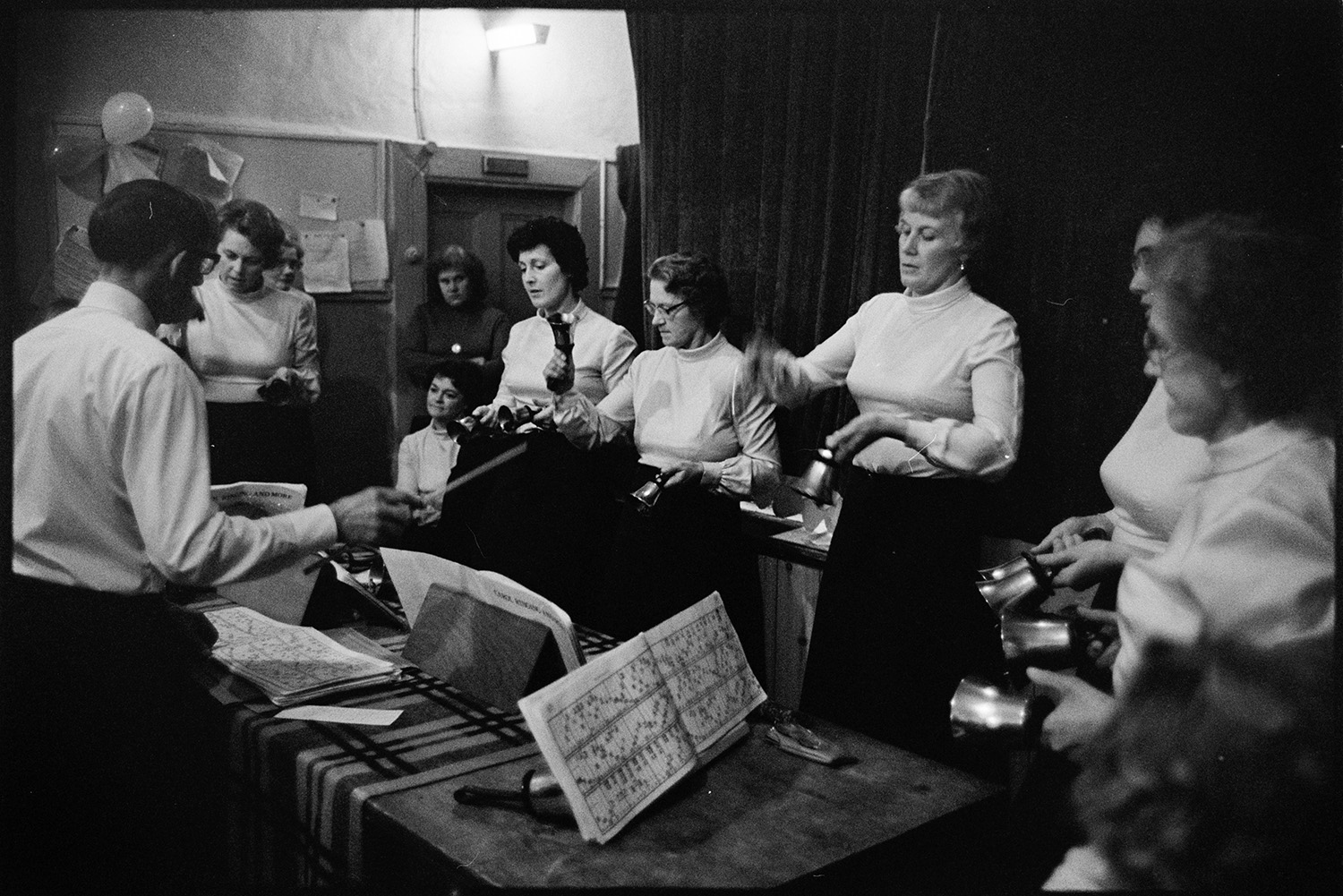 Christmas Show in village hall Hand bell ringers.
[Group of women in the Ashreigney Hand bell Ringers performing at the Christmas Show in Merton Village Hall, being conducted by a man.]