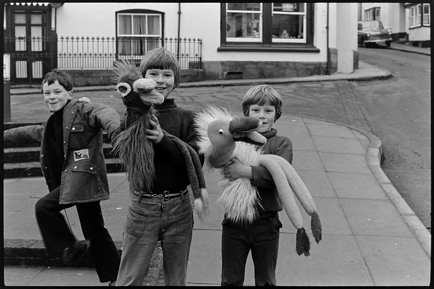 Children with glove puppets in street. <br />
[Three children in the centre of Hatherleigh with two hand puppets based on the Emu puppet used by the comedian Rod Hull.]