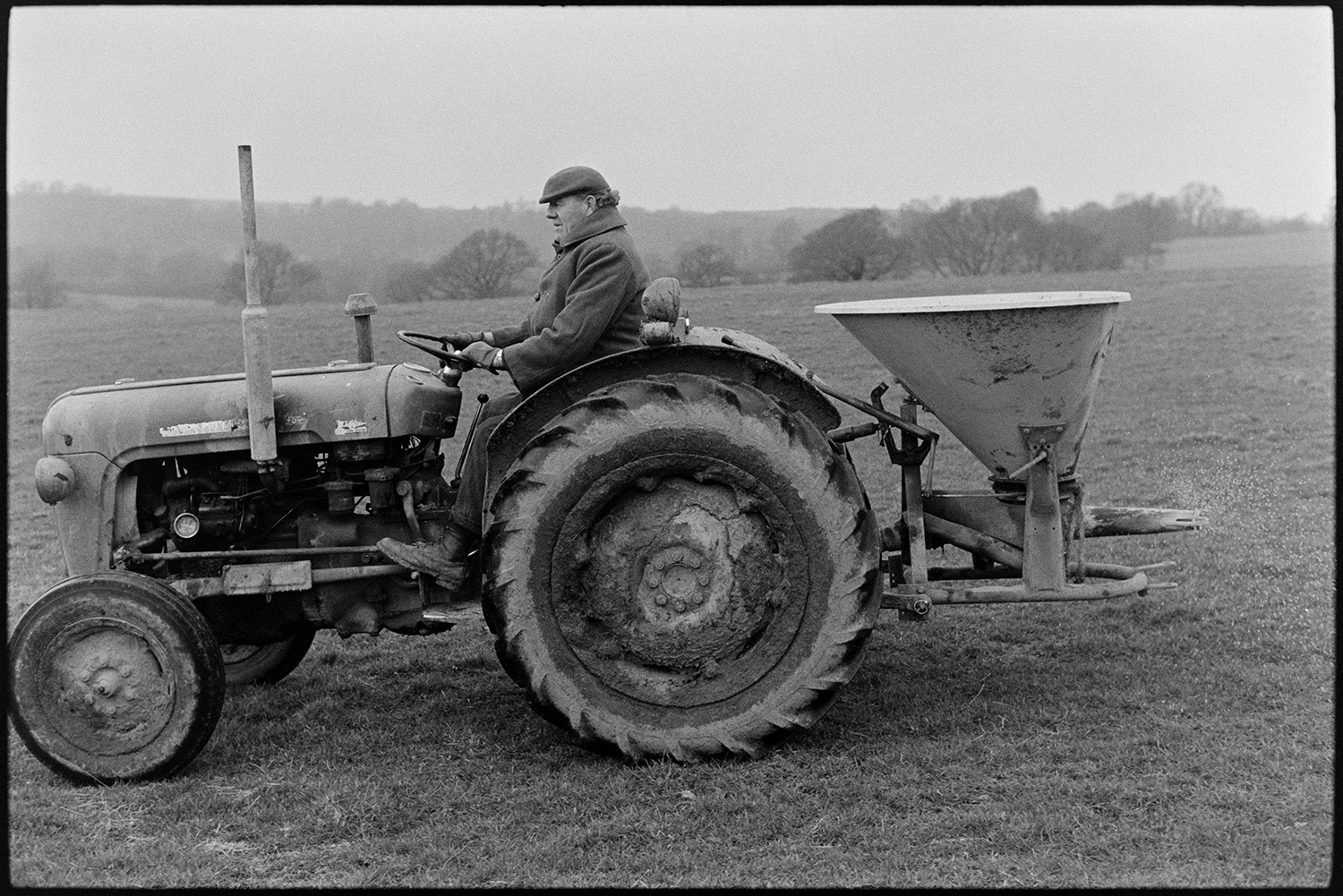 Man loading up and spreading fertilizer. <br />
[John Ward driving a tractor and spreading fertilizer in a field at Parsonage, Iddesleigh.]