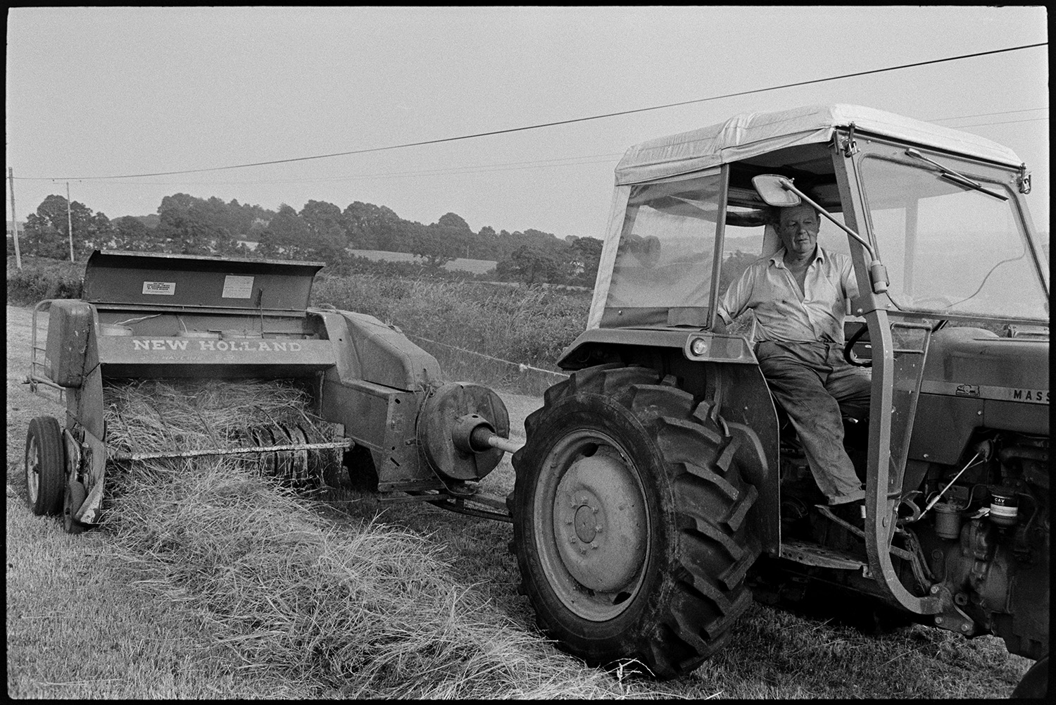 Farmers baling hay. 
[John Ward driving a tractor and baler in a field at Parsonage, Iddesleigh.]
