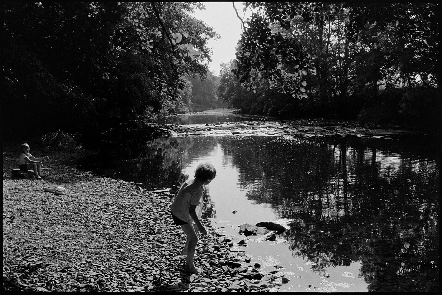 People beside river. 
[Two boys playing on the banks of the River Torridge at Halsdon, Dolton. One boy is skimming a stone.]