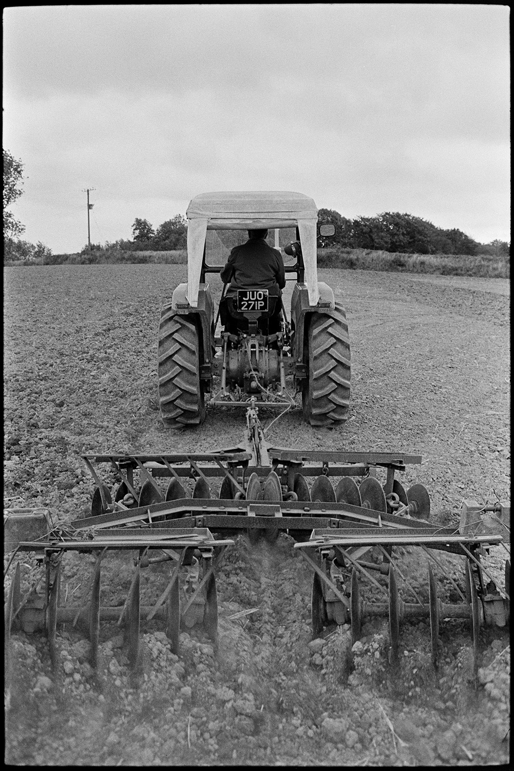 Harrowing field. 
[John Ward driving a tractor pulling a harrow over a field at Parsonage, Iddesleigh.]