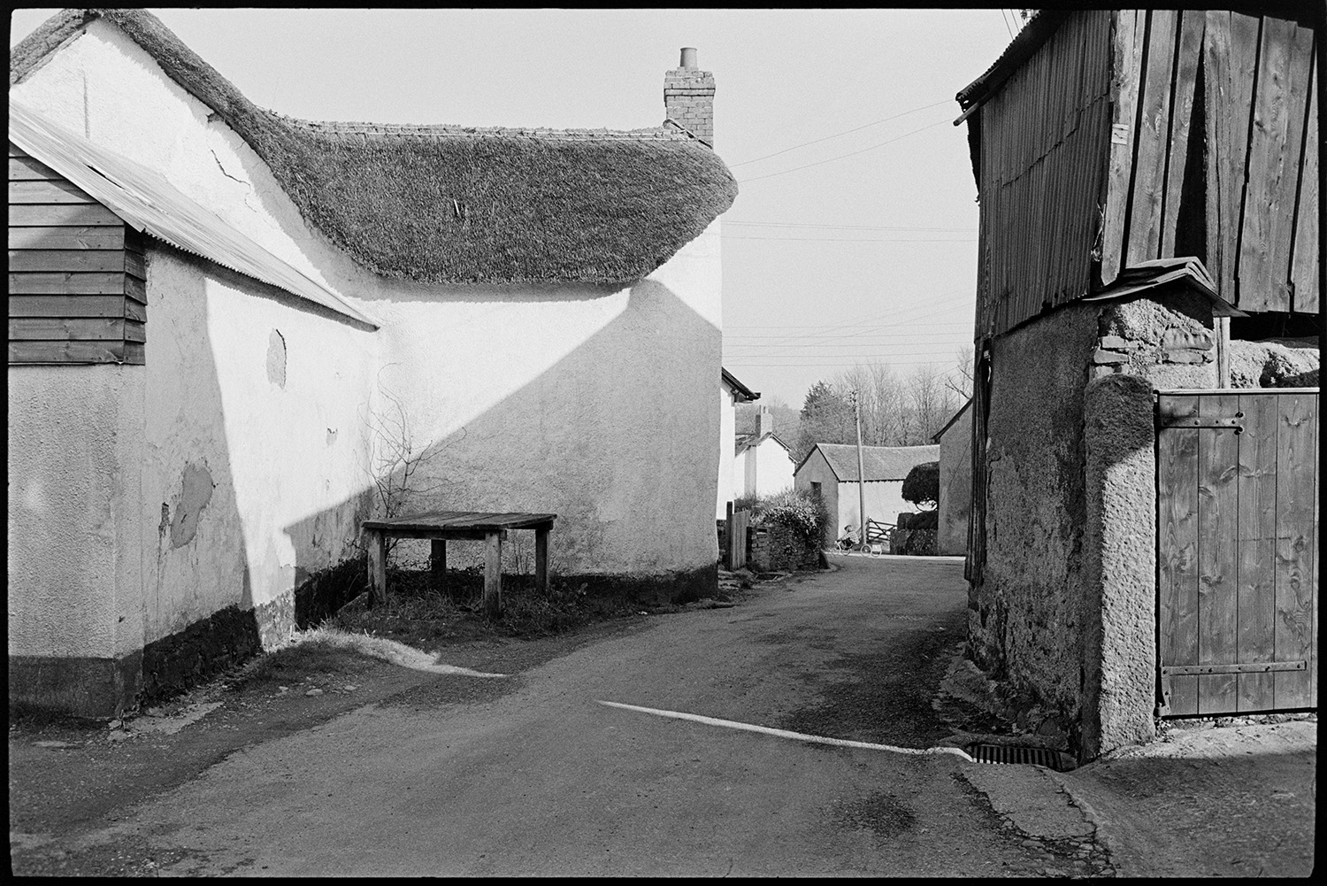 Street scenes, washing on line. 
[A street in Kings Nympton with a cob and thatch cottage and a wooden barn. A wooden stand, possibly a milk churn stand is by the cottage.]