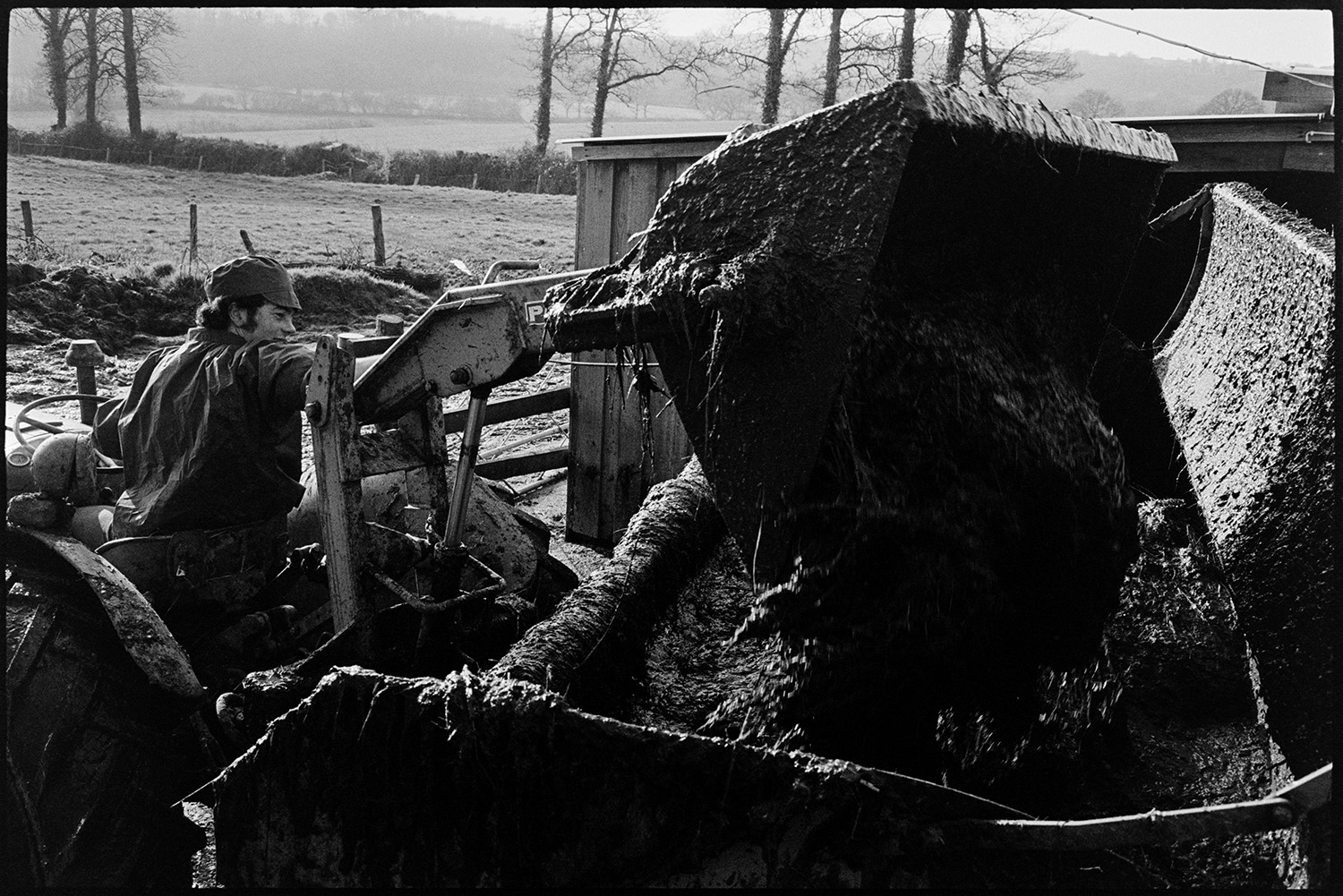 Tractor and muck spreader. 
[David Ward loading dung into a muck spreader using a tractor at Nethercott, Iddesleigh.]