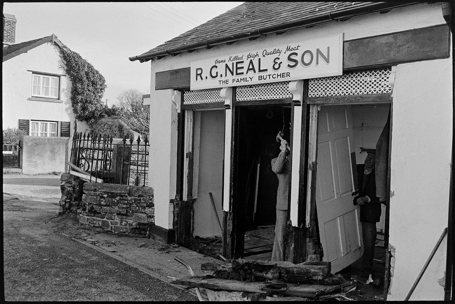 Renovation front of butchers shop. 
[A man knocking down the front of R G Neal & Son butcher's shop in Dolton, before refurbishing it. The sign is above the shop.]