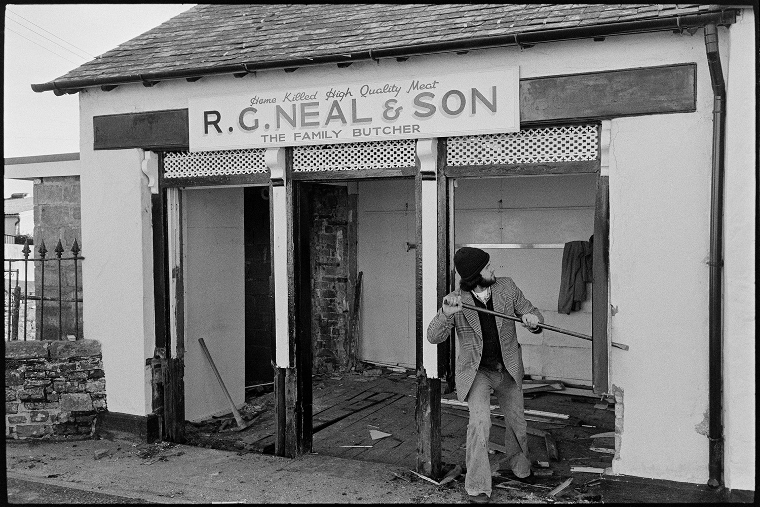 Renovation front of butchers shop. 
[A man knocking down the front and interior of R G Neal & Son butchers shop in Dolton, before refurbishing it. The sign is above the shop.]