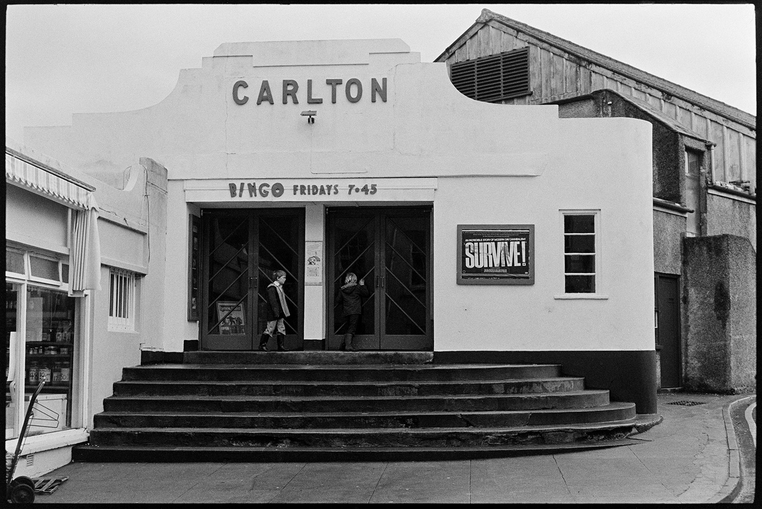 Front of Cinema. 
[Two children looking in the front doors of the Carlton cinema in Okehampton. An advert for bingo on Friday evenings is above the doors.]