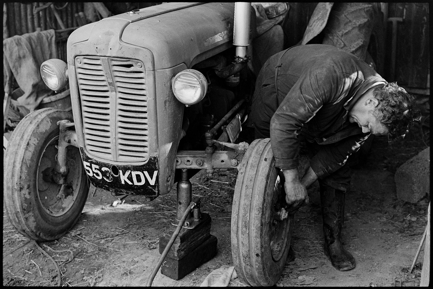 Mechanic mending puncture in tractor tyre. 
[Cyril Dunn fixing a puncture in a tractor tyre at Parsonage, Iddesleigh.]