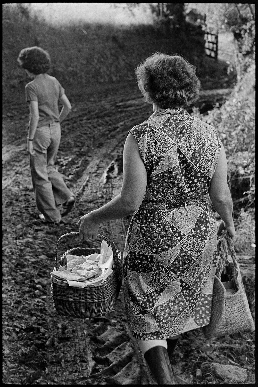 Woman taking tea to farmers in field. 
[Hettie Ward and Elizabeth Ward walking along a muddy track at Parsonage, Iddesleigh, taking a basket of food to farmers working in the fields.]