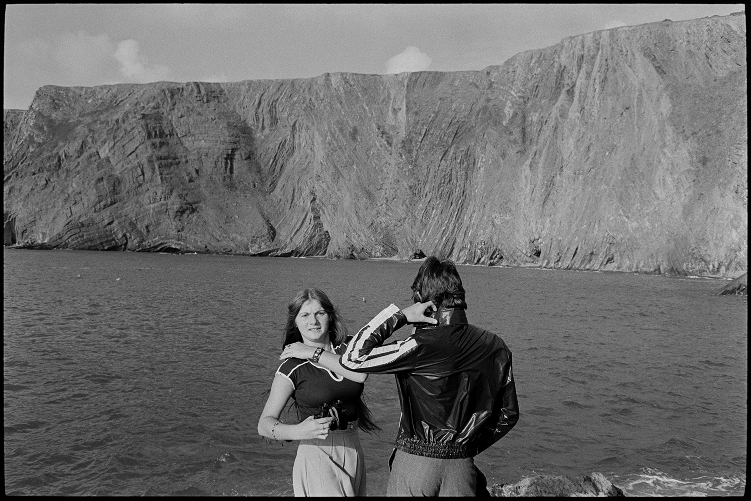 Couple in front of sea and cliff. 
[A man and woman stood by the sea and cliffs at Hartland.]