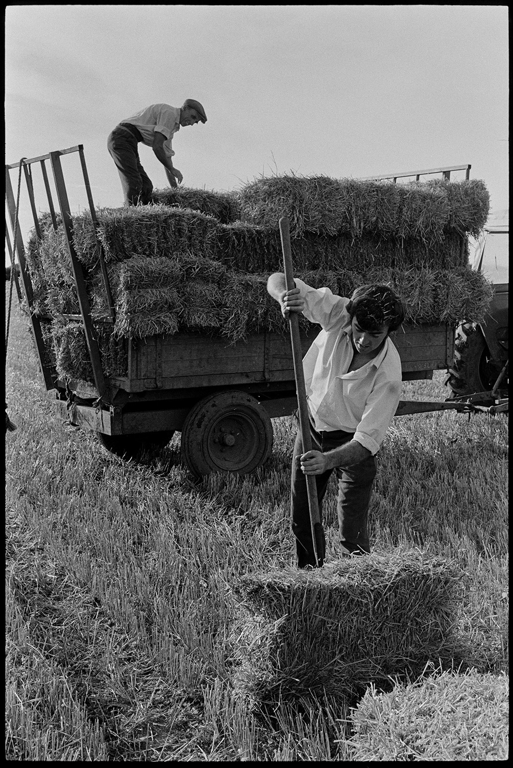 Two members of the Ward family loading straw bales onto a trailer in a field at Nethercott, Iddesleigh, using a pitchfork.