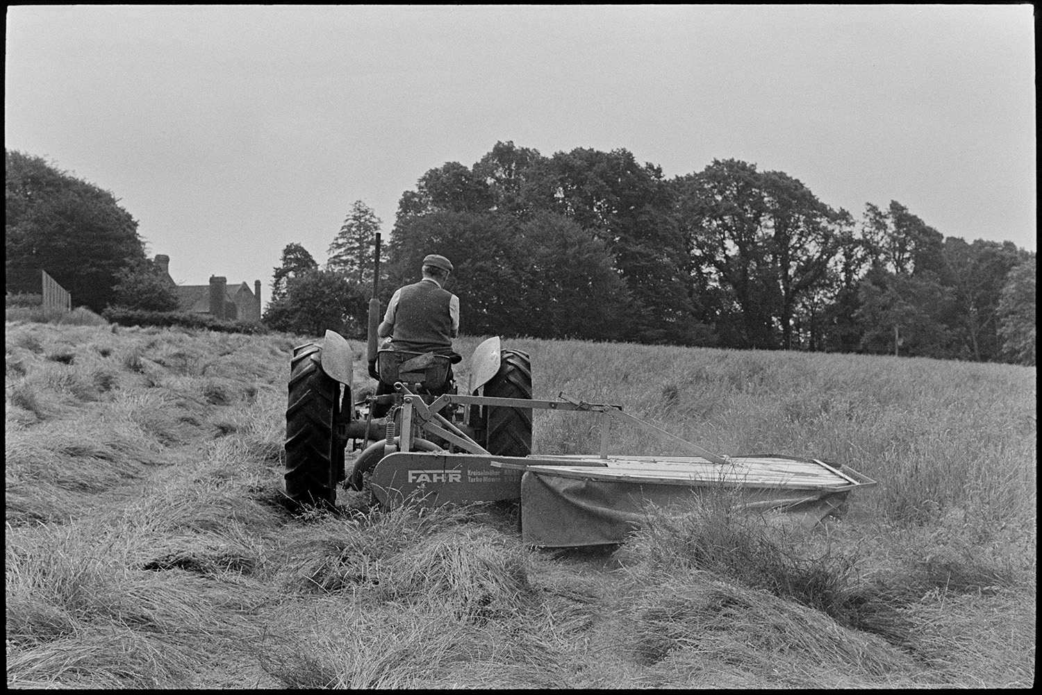 Grass cutter and tractor, farmer checking. 
[John Ward mowing a field with a grass cutter and tractor at Parsonage, Iddesleigh.]