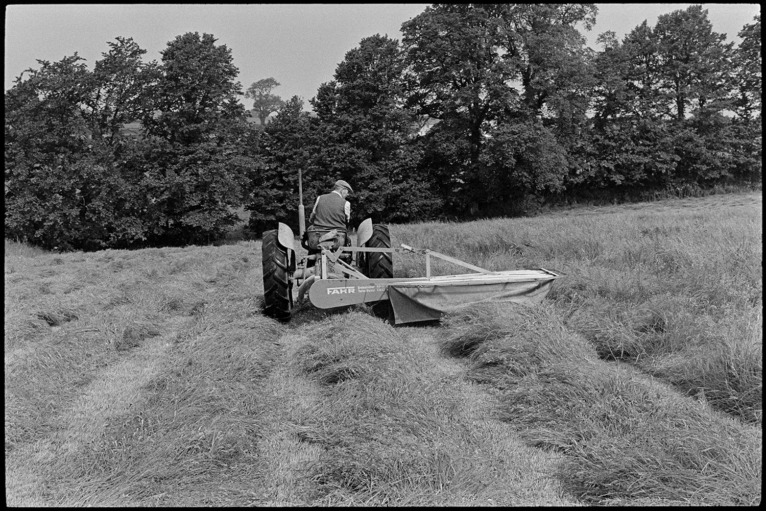 Cutting grass. 
[John Ward mowing a field with a grass cutter and tractor at Parsonage, Iddesleigh.]