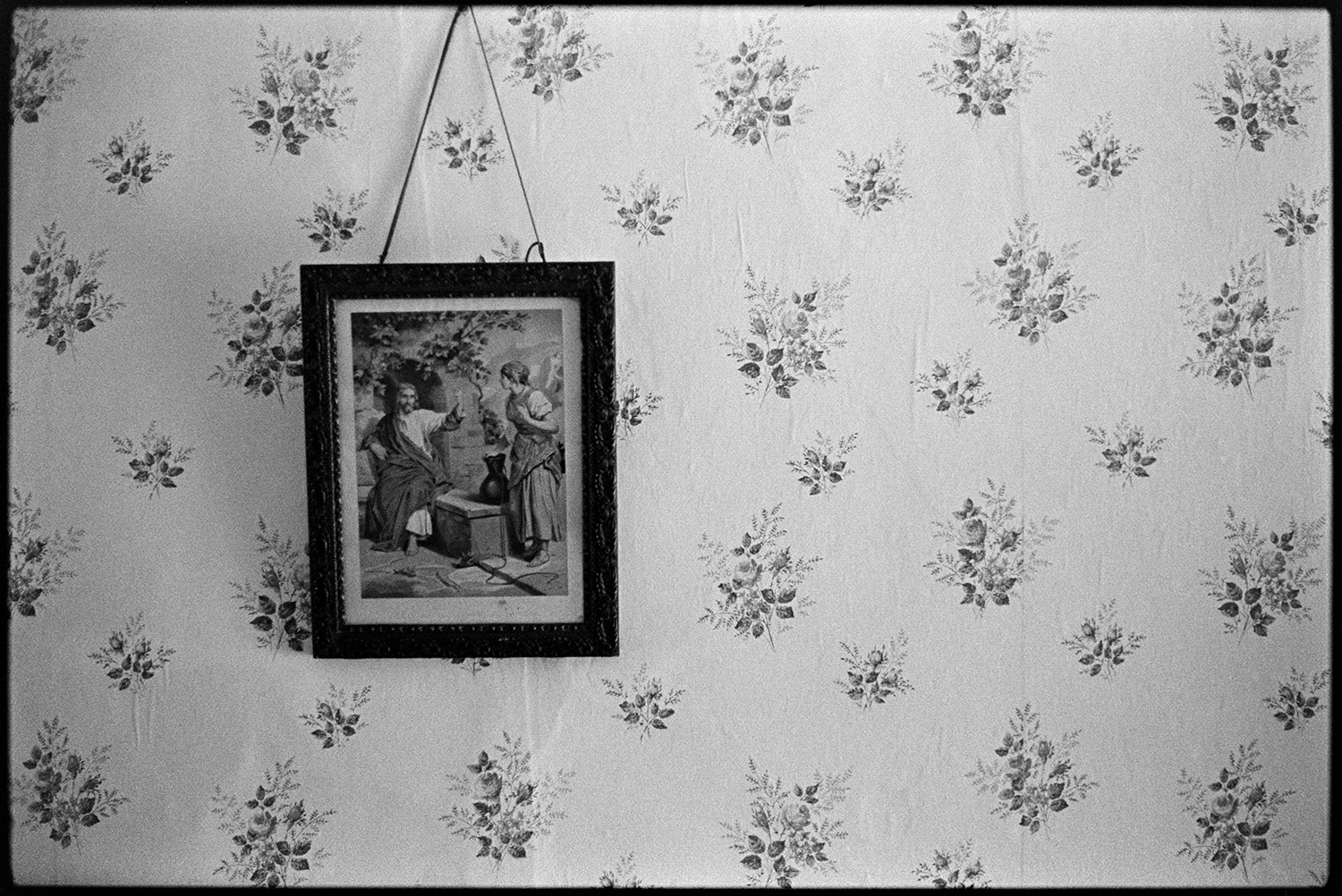 Religious picture on bedroom wall. 
[A religious framed picture hung on a wall in Emily Easterbrook's house at West Lane, Dolton. The wall is covered with floral patterned wallpaper.]