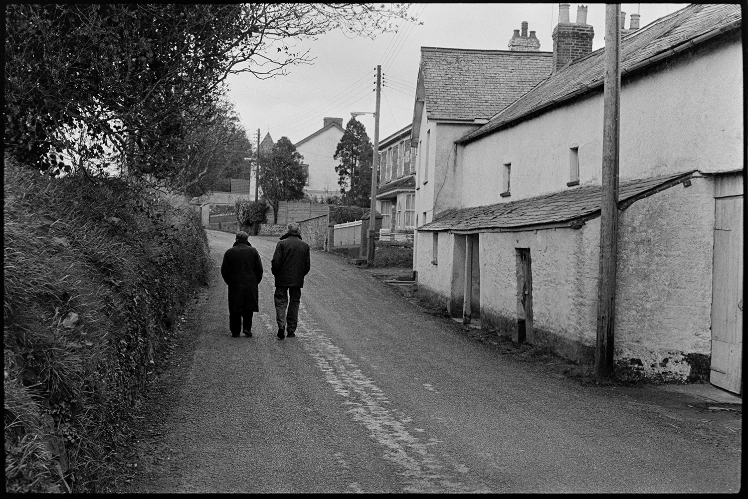 Street scene with porch. 
[Two men walking along Rectory Road, Dolton. Cottages are visible on the right of the road and a hedgebank is on the left.]