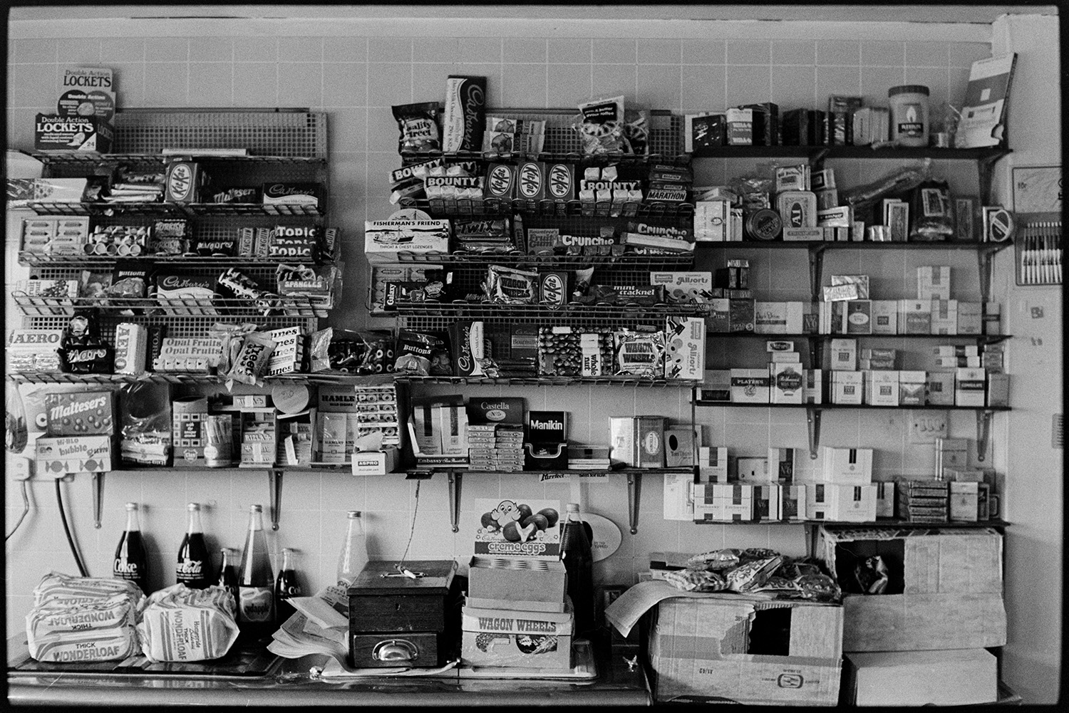 Interior of cafe at garage, sweets and soft drinks on shelf. 
[The shelves behind the counter in the café at Fishleigh Rock Garage, Umberleigh. They are stacked with sweets, chocolate bars, fizzy drinks and cigarettes, amongst of the good.]