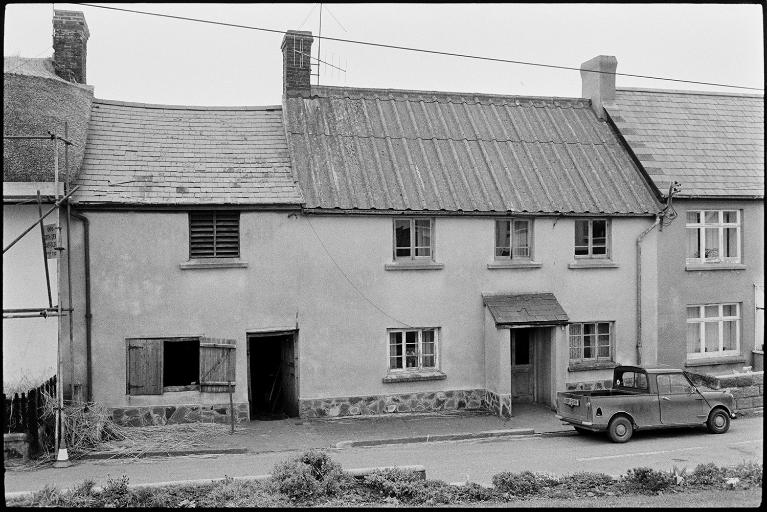 Cottages with blacksmiths shop. 
[Cottages with slate, corrugated iron and thatched roofs on a street in Atherington. The cottage with wooden shutters and slats is Mr Loosemore's Blacksmith's workshop.]