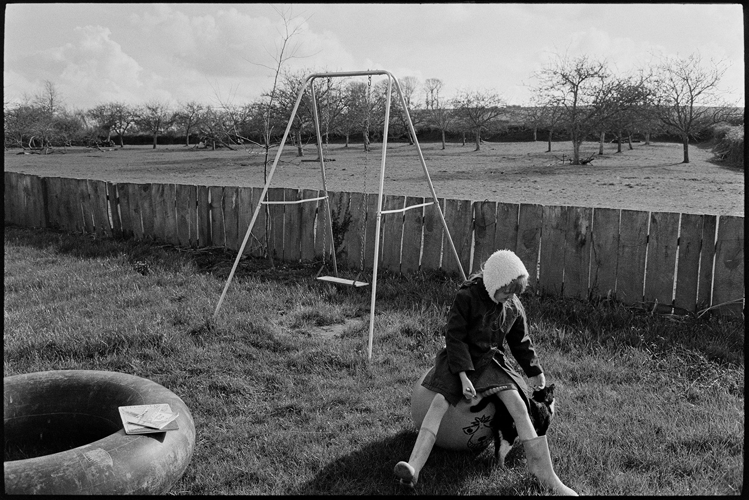 Cob and thatch barn, collapsing. 
 [A girl sat on a space hopper and stoking a cat in the garden at Higher House Farm, Atherington. A swing and rubber ring are behind her and an orchard can be seen in the background behind the garden fence.]