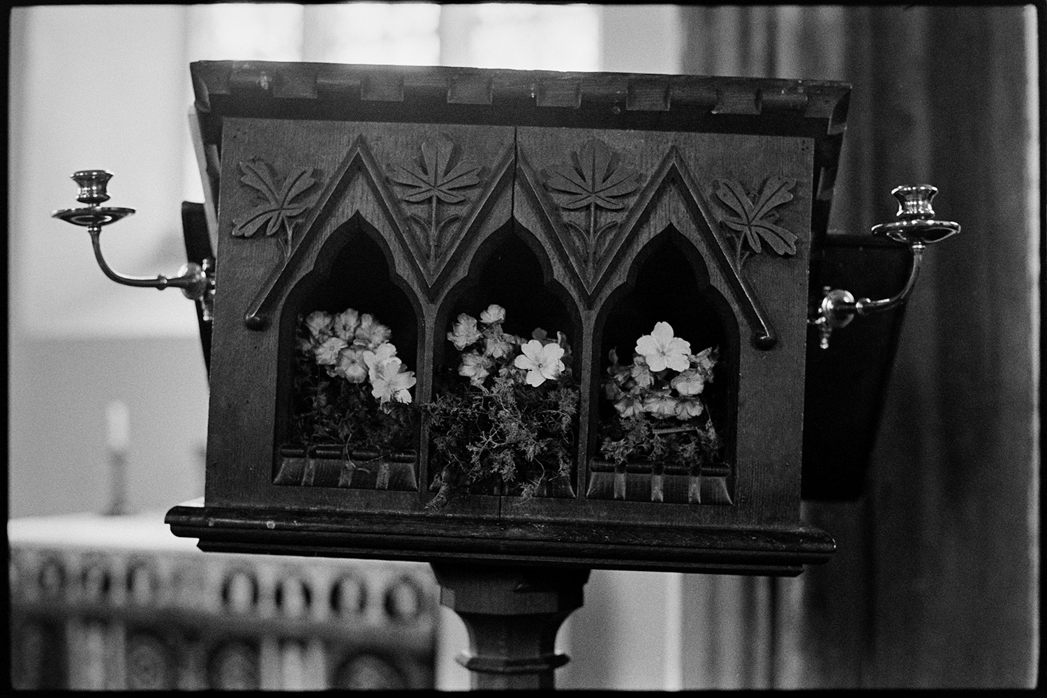 Easter flowers on lectern and with hymn books. 
[The lectern in Dowland Church decorated with flowers for Easter. It also has a carved leaf decoration and two candlesticks attached.]