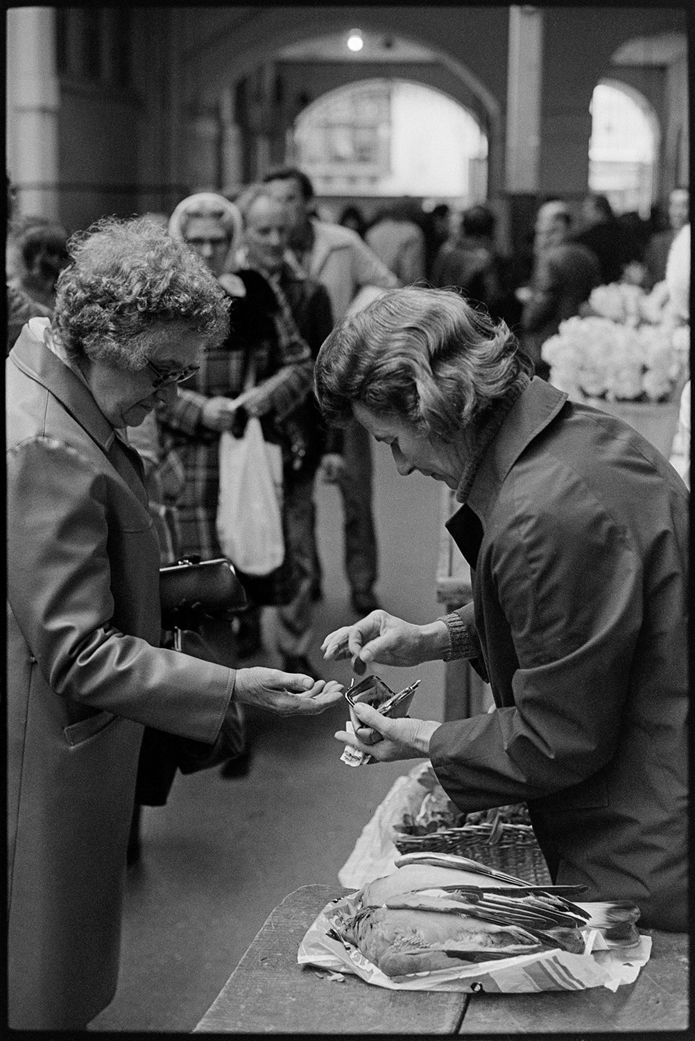 British Legion and other stalls in Pannier Market. 
[A woman giving a customer change for an item she has bought from her stall in Barnstaple Pannier Market. Two birds, possibly pigeons, can be seen on the stall.]