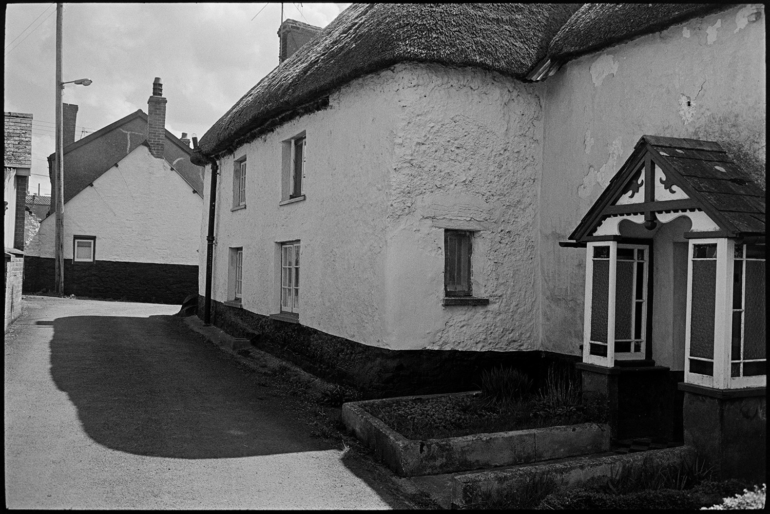 Street scenes with horse, cob and thatched cottages, porch. 
[A cob and thatch cottage with an ornate porch, on a street on Kings Nympton.]