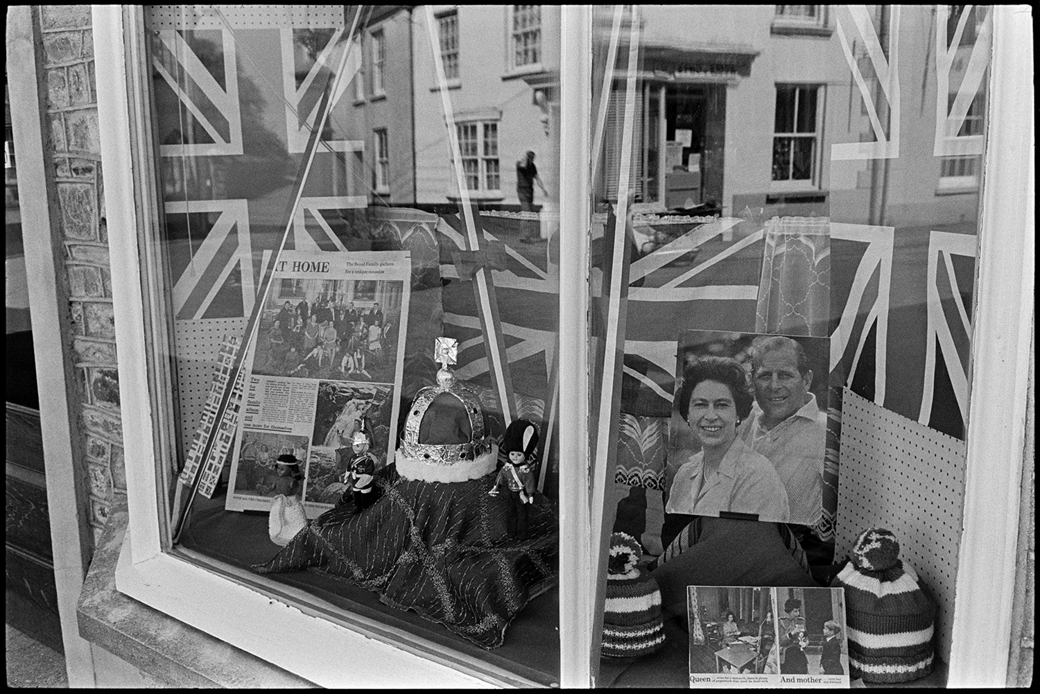 Grocery store decorated for jubilee. 
[The shop front window of Knights Grocery Store in Fore Street, Chulmleigh, decorated for Queen Elizabeth II Silver Jubilee. It contains Union Jack flags, a model crown and pictures of the Queen.]